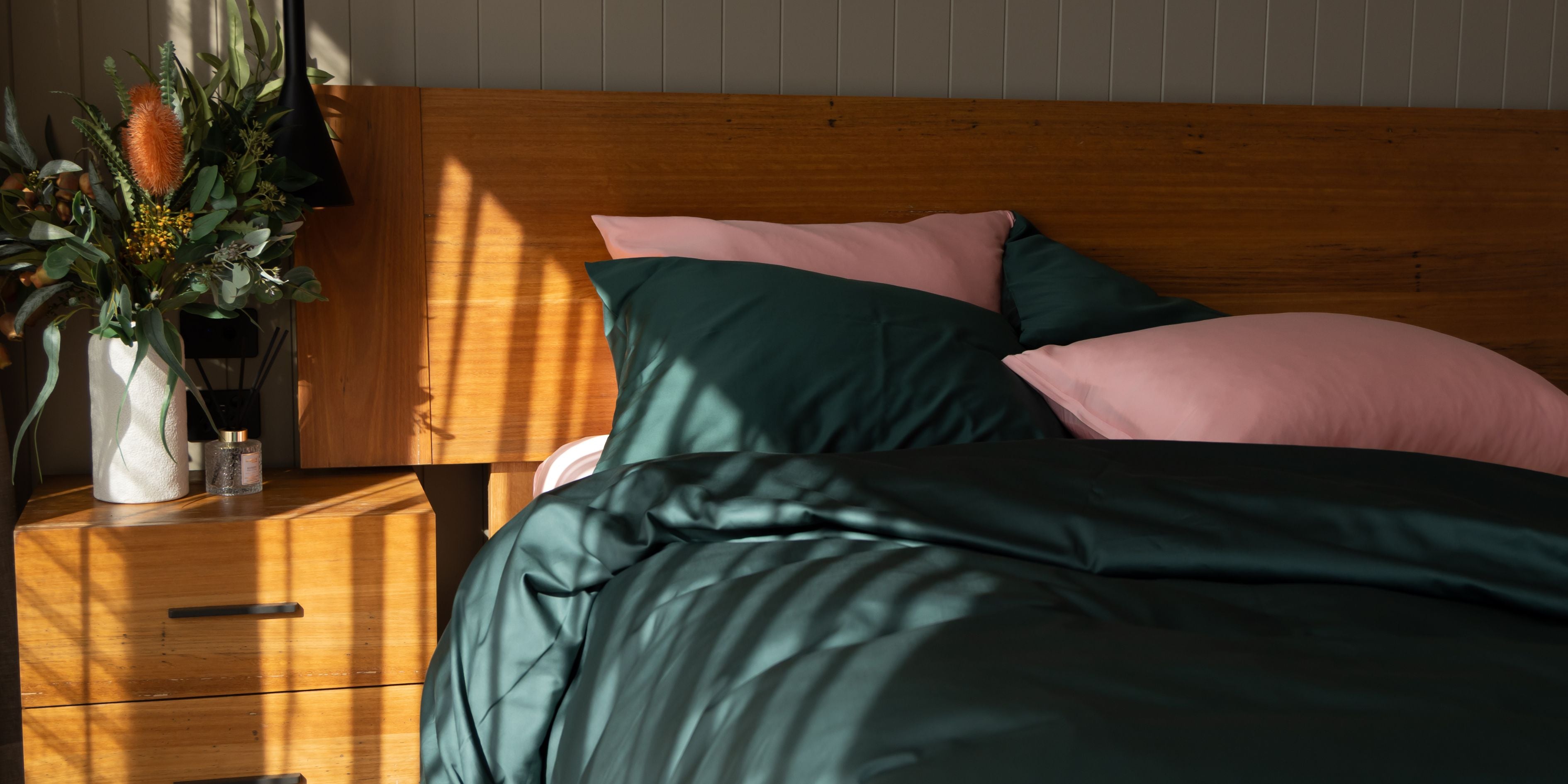 Bedroom with wooden headboard, green and pink bedding, and a nightstand with flowers.