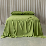 Green bedspread on a bed with matching pillows against a neutral curtain background.