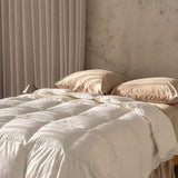 Beige quilt insert and pillows on a bed with a neutral wall and curtain in the background.