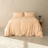 Peach-colored quilt cover set made up on a double bed with two matching pillowcases against a neutral concrete wall