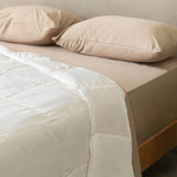 Beige bed with white quilt insert and pillows on a neutral background.