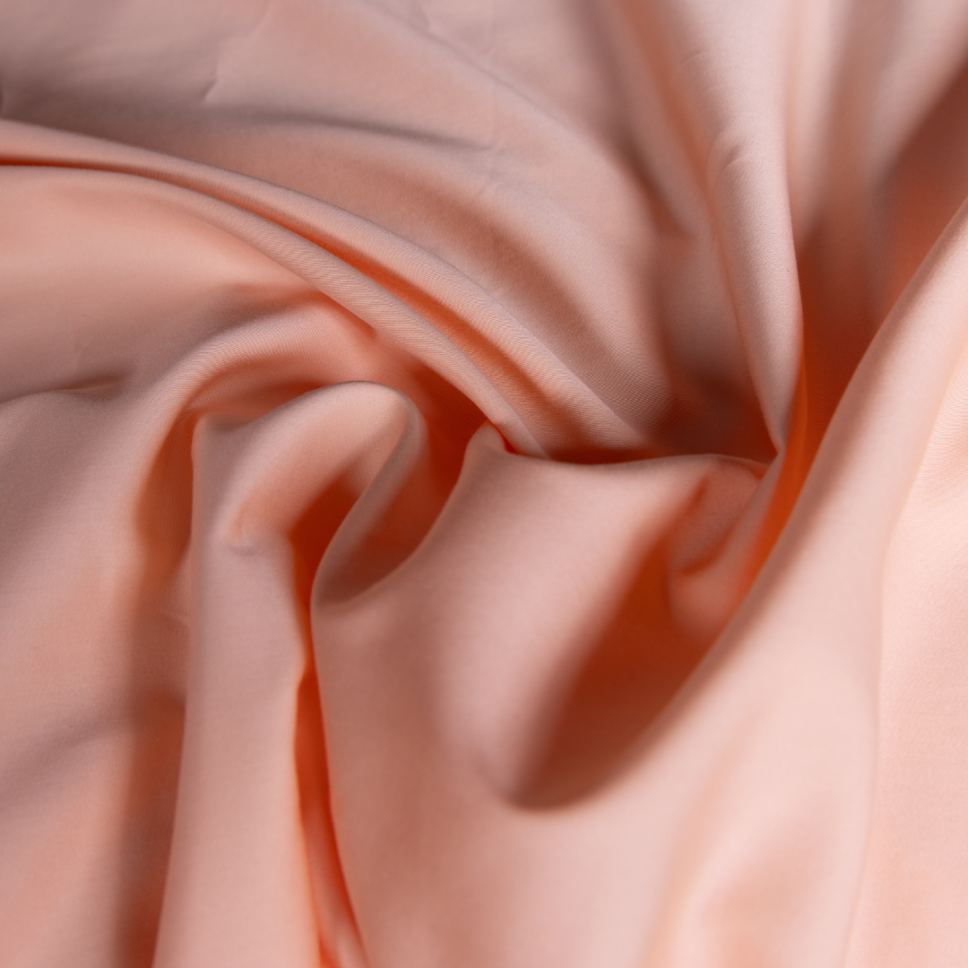 Close-up of peach-coloured sheet fabric showing its smooth, silky texture – ultra-soft, breathable material designed for a luxe, comfortable night’s sleep.