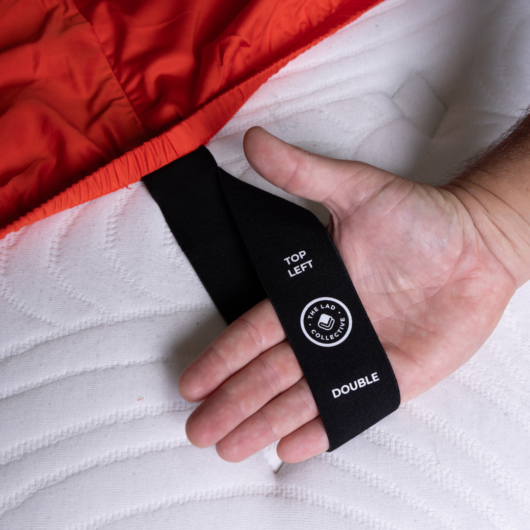 Close-up of TLC logo tag on red bamboo cotton fitted sheet showing brand quality.