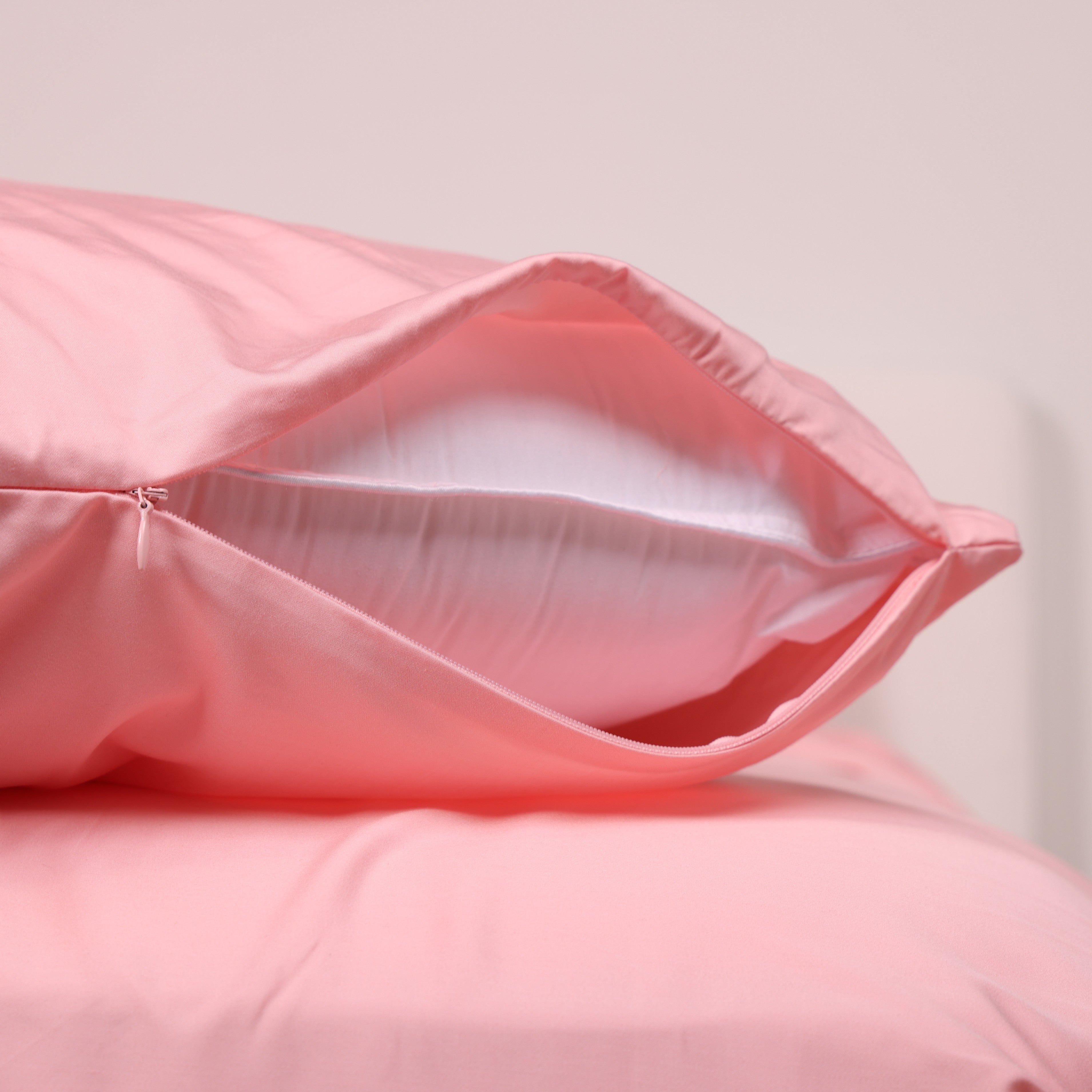 A pink bed with matching pillows and wooden bedside tables with small plants.