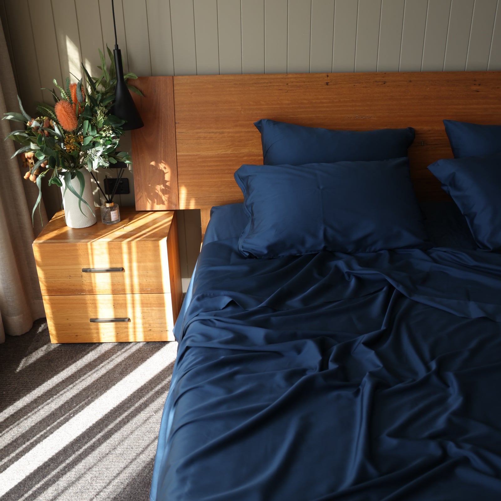 Bed with blue bedding and pillows next to a wooden cabinet with a mirror and decorative items.