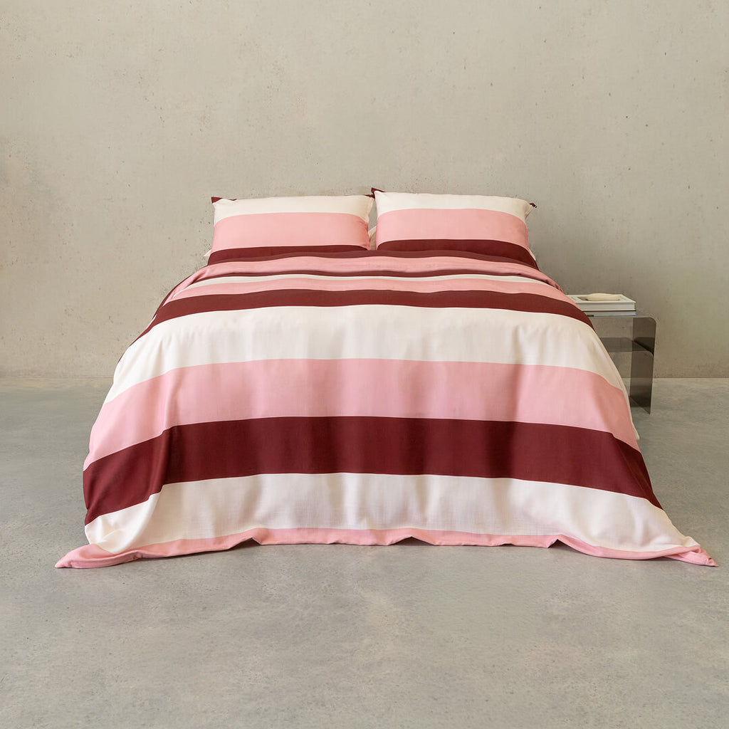 Pink, blush, cream, and burgundy striped quilt cover set with matching pillowcases displayed on a neatly made bed in a modern minimalist bedroom.