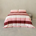 Pink, blush, cream, and burgundy striped quilt cover set with matching pillowcases displayed on a neatly made bed in a modern minimalist bedroom.