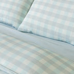 Close-up of light blue gingham bedding with matching pillowcases and a soft blue fitted sheet, highlighting the subtle check pattern and coordinated color palette