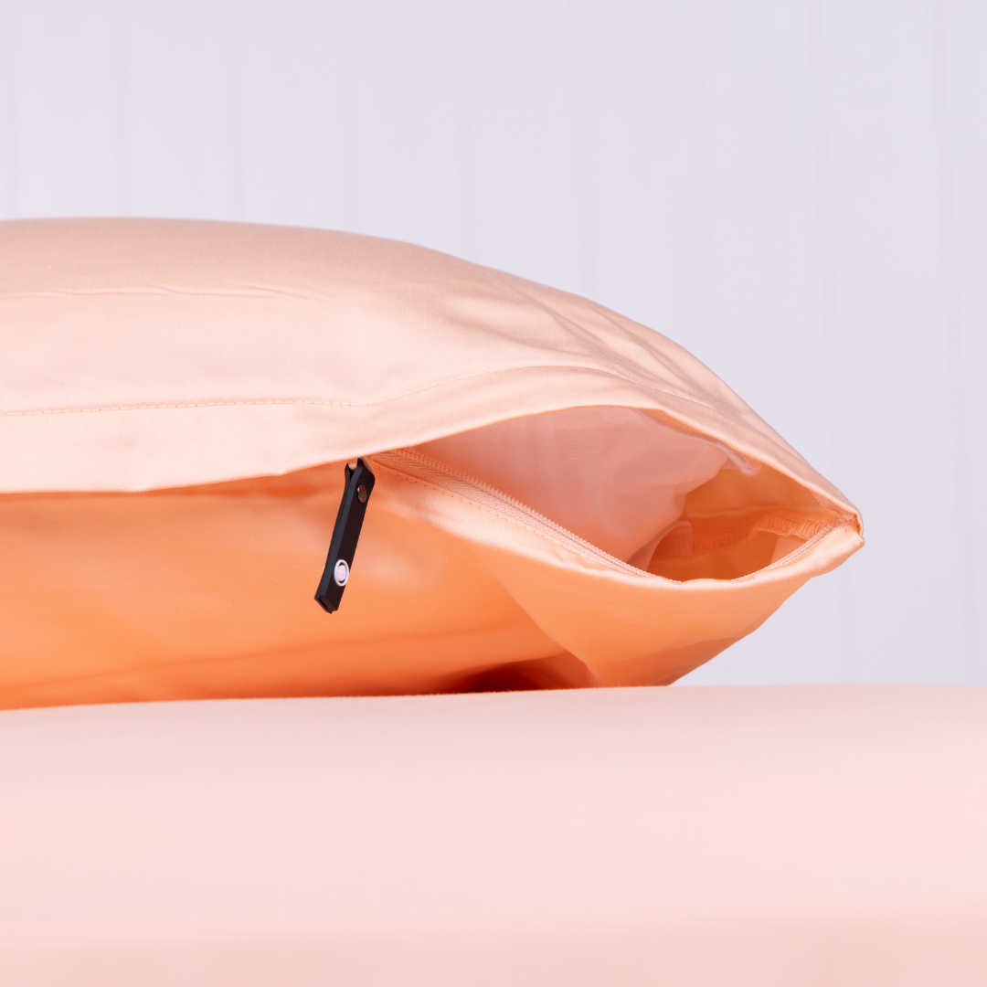 Close-up of a peach-coloured pillowcase featuring a discreet zipper closure with a black pull tab, displayed on matching bedding.