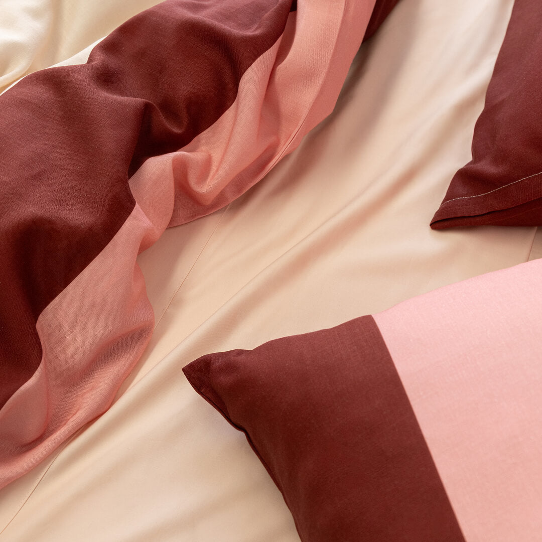 Pink, cream, and burgundy striped quilt cover and pillowcases layered over soft neutral sheets, highlighting the fabric drape, texture, and warm color palette.