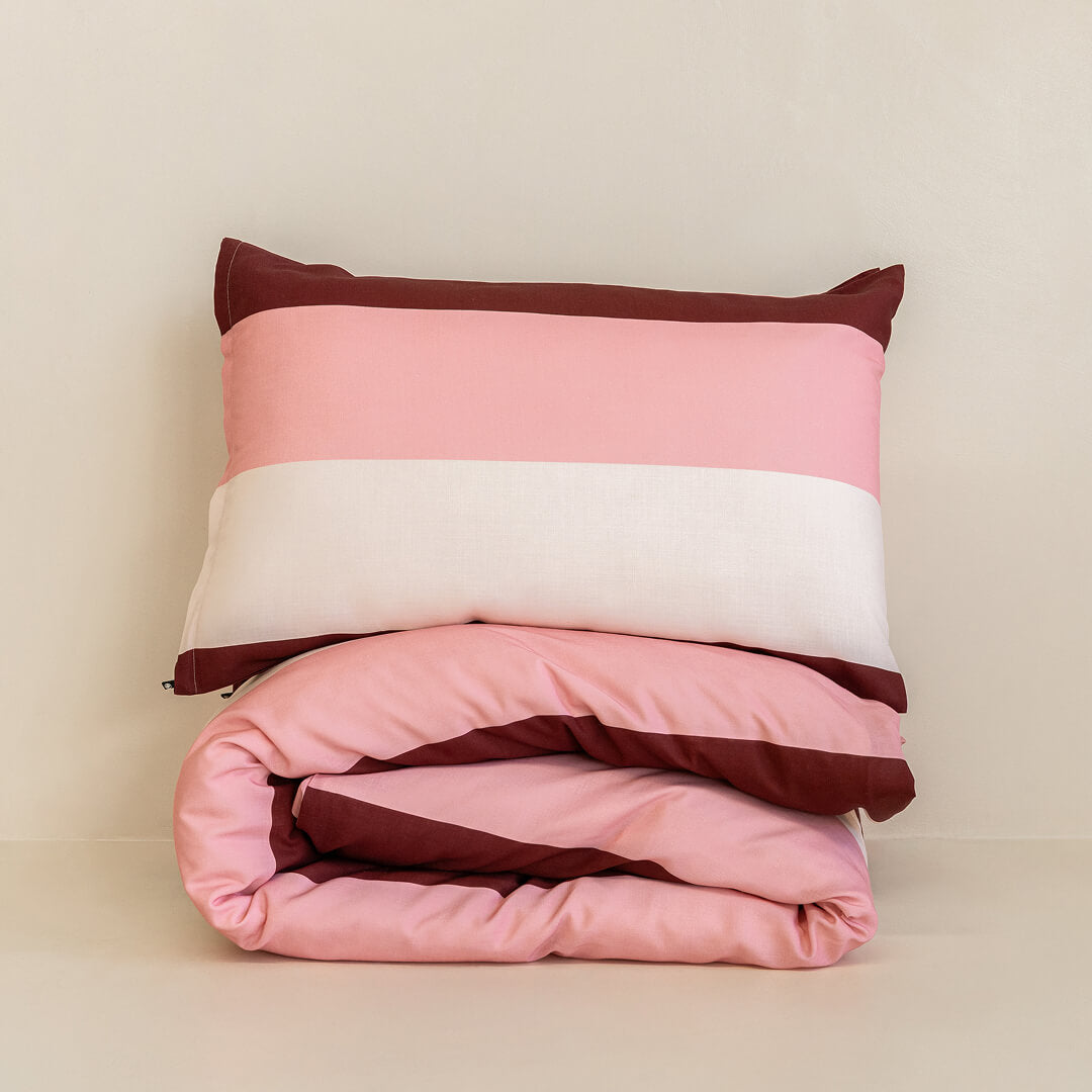 Folded striped quilt cover set with a matching pillowcase in blush pink, cream, and burgundy tones, neatly stacked to showcase the bold stripe pattern and soft fabric.