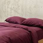 Burgundy bedding set with two pillows on a bed against a neutral wall.