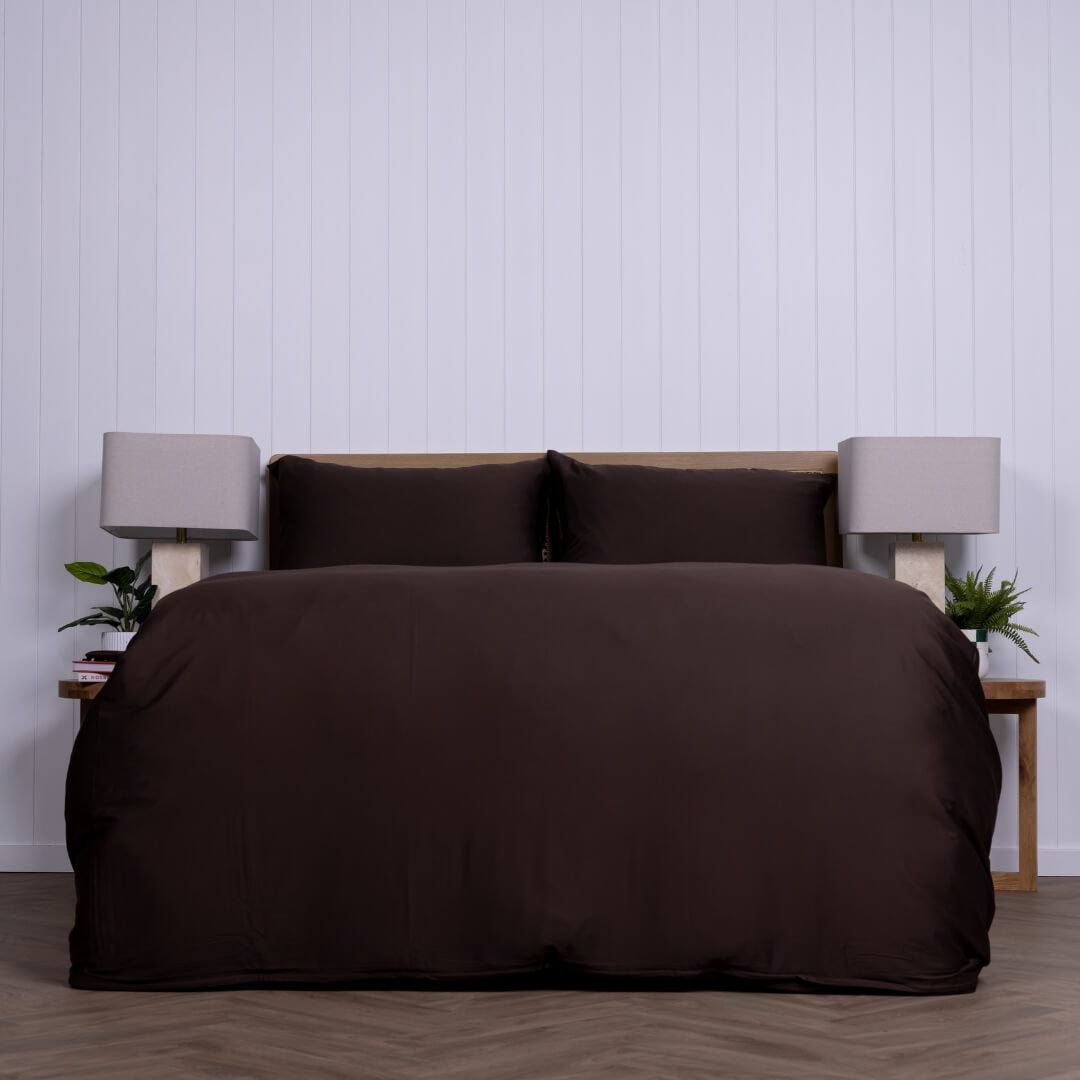 Brown bedspread set on a bed with matching pillows against a white panelled wall.