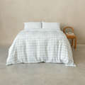 Light blue gingham quilt cover set with matching pillowcases displayed on a neatly made bed, styled in a minimalist bedroom with a woven wooden chair and neutral textured wall