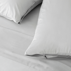 Close-up of light gray pillowcases with concealed zipper closures and small black zipper pulls on matching bedding.