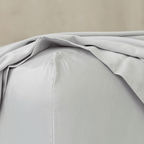 Close-up of a light gray flat sheet draping softly onto a concrete floor, showing its smooth texture and flowing folds.