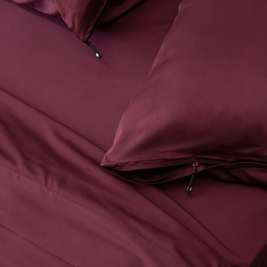 Close-up of burgundy bedding with a pillow and fitted sheet.
