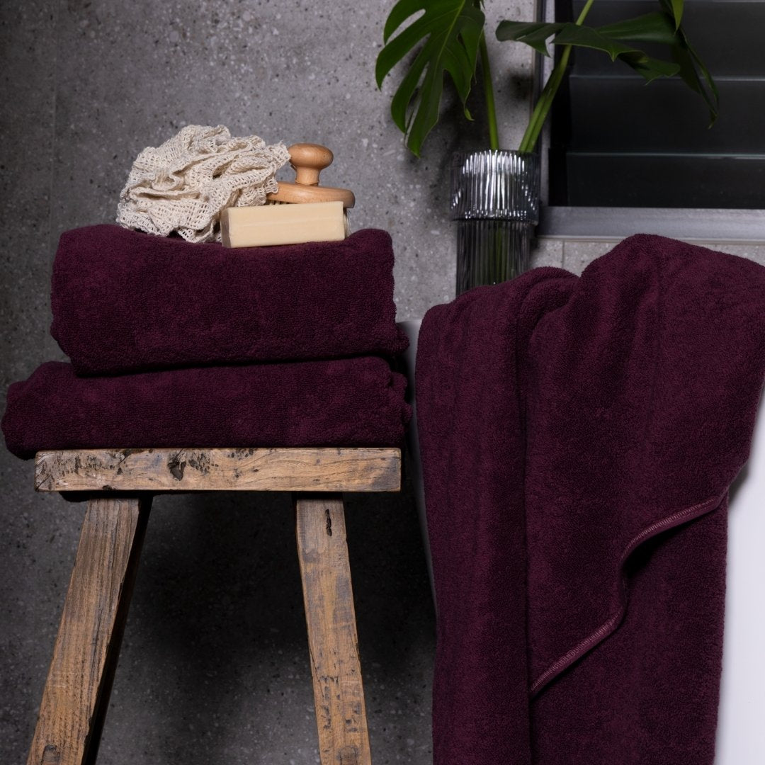 Burgundy towels on a wooden stool with a plant in the background.