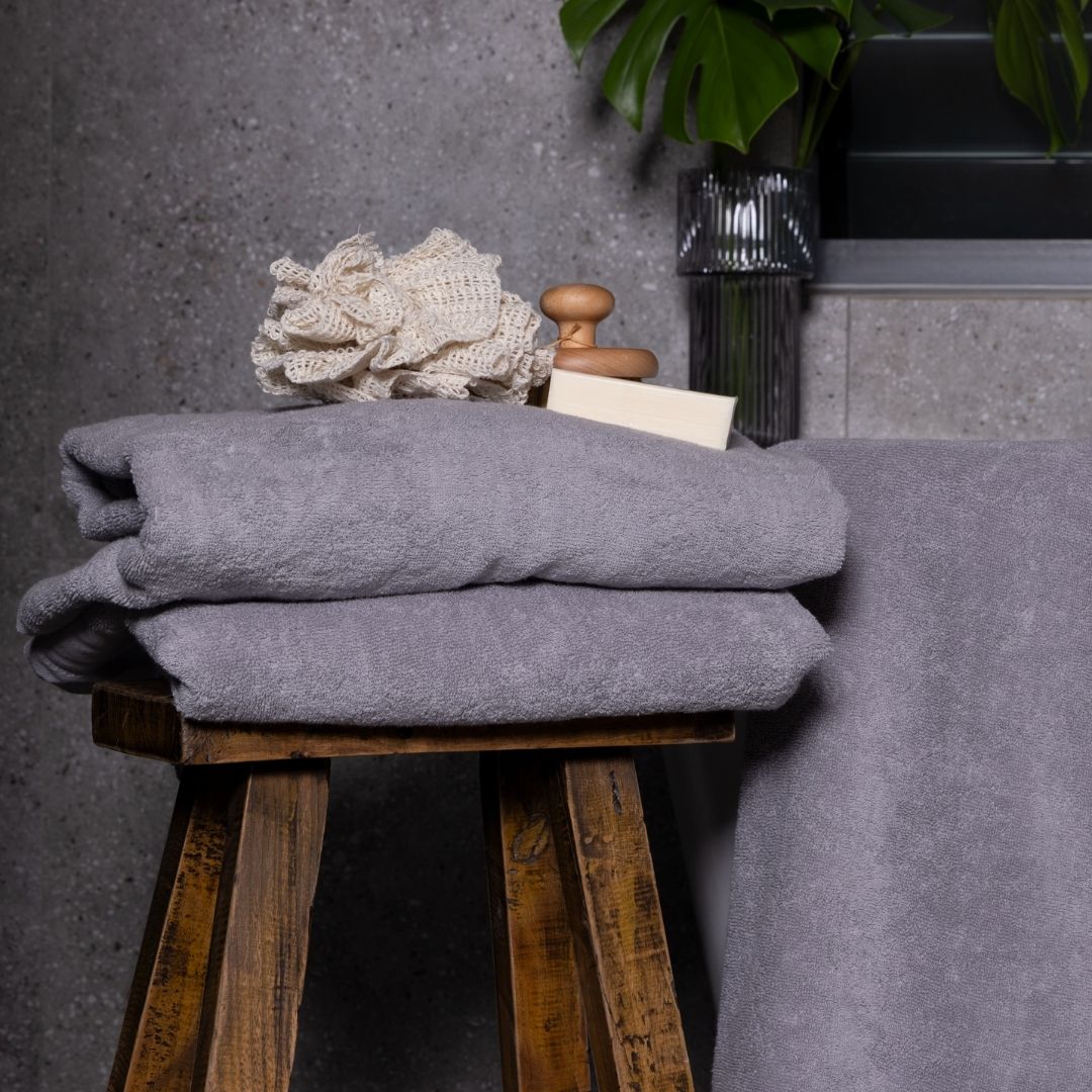 Stack of gray towels on a wooden stool with decorative items against a gray wall.