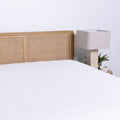 Bed with wicker headboard and white mattress protector, nightstand with lamp in the corner.