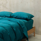 Teal bed sheets and pillows on a wooden bed against a neutral wall.
