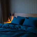 Bed with blue bedding and pillows in a dimly lit bedroom.