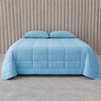 Blue quilted cooling blanket on a bed with beige curtains in the background.