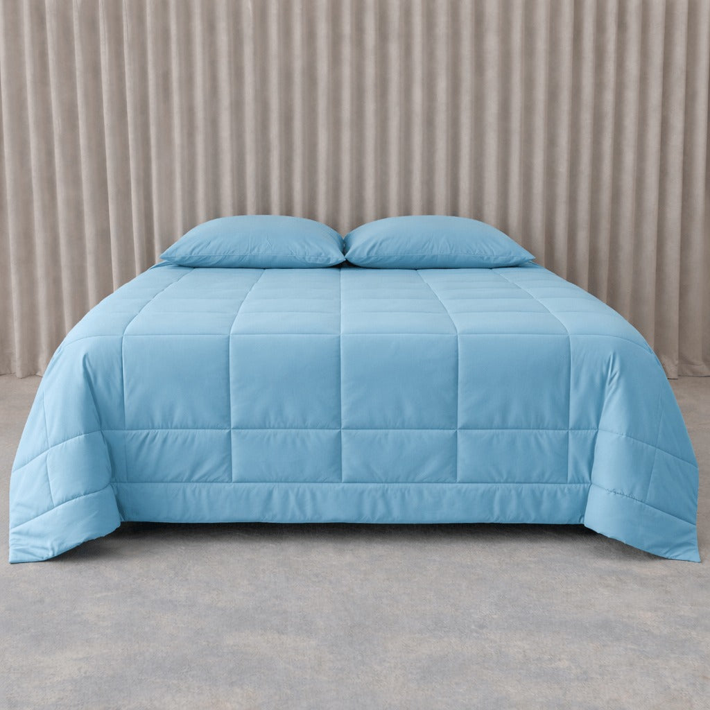 Blue quilted cooling blanket on a bed with beige curtains in the background.