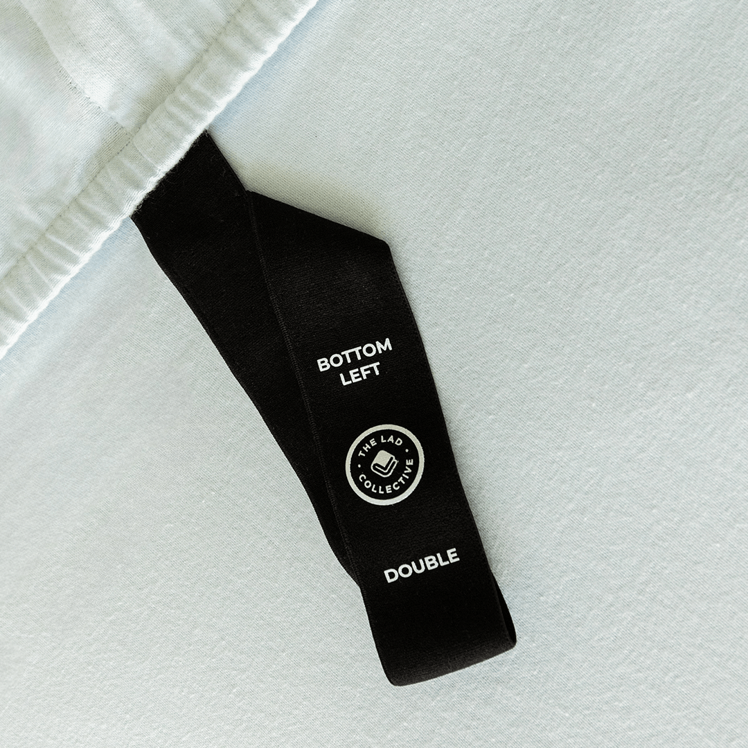 Close-up of a fitted sheet orientation tag labeled “Bottom Left,” designed to make bed-making easier and ensure correct sheet placement.