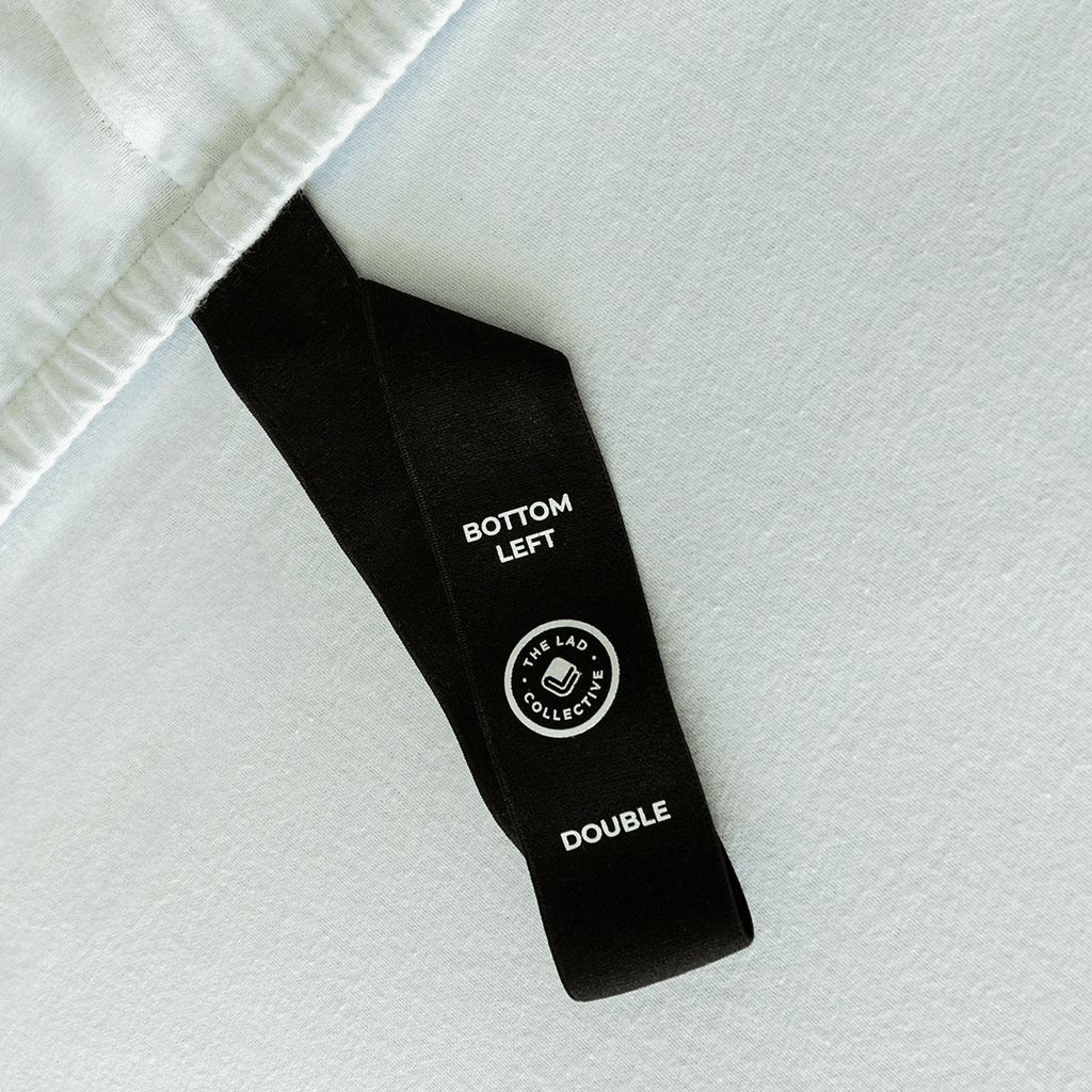 Close-up of a fitted sheet orientation tag labeled “Bottom Left,” designed to make bed-making easier and ensure correct sheet placement.