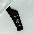 Close-up of a fitted sheet orientation tag labeled “Bottom Left,” designed to make bed-making easier and ensure correct sheet placement.