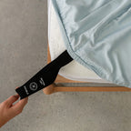 Person holding a black strap with a brand logo over a light blue fitted sheet.