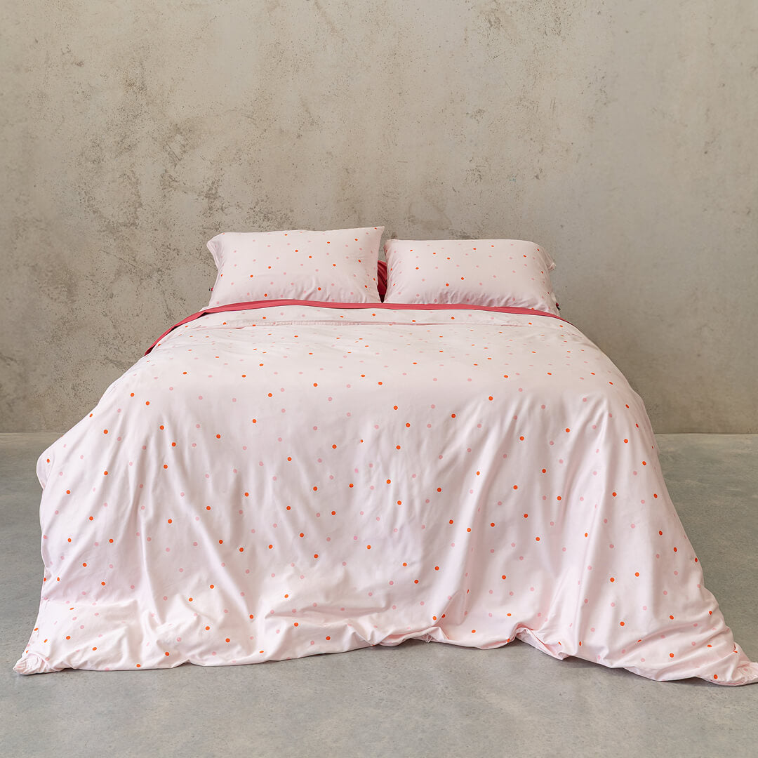 Pink polka dot bedding set on a bed against a grey wall.