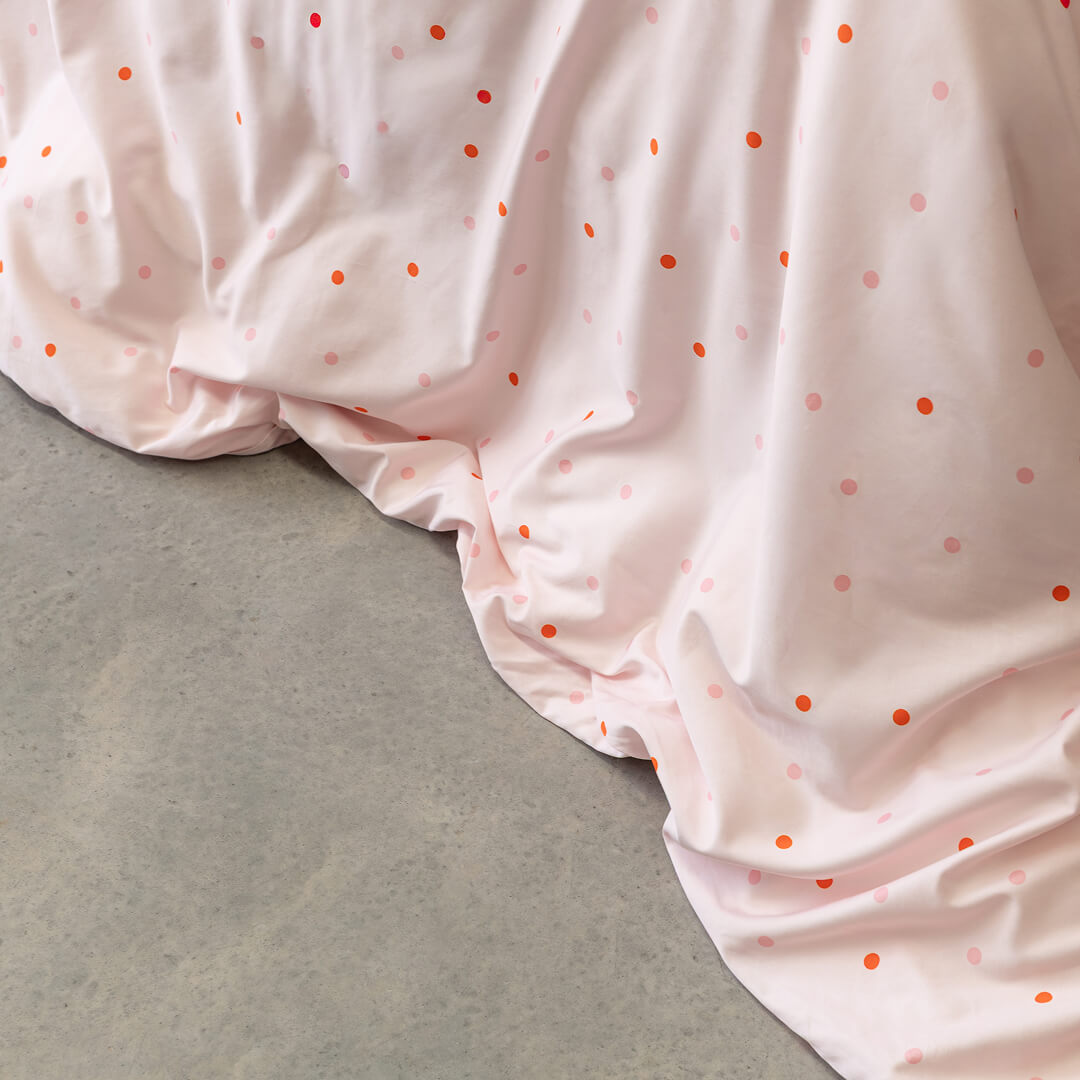 Pink polka dot quilt cover on a bed with a grey concrete floor.
