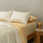 Angle view of a double bed styled with a yellow floral pattern quilt cover over a solid yellow sheet set