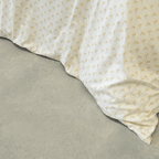 Close-up view of cream floral print quilt cover fabric draping smoothly onto a light gray concrete floor