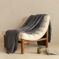 Charcoal coloured cooling blanket draped over a fashionable lounge chair. 