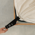 Beige fitted sheet with an extended orientation tag at the mattress corner, demonstrating the easy-to-locate labeling system for faster bed setup.