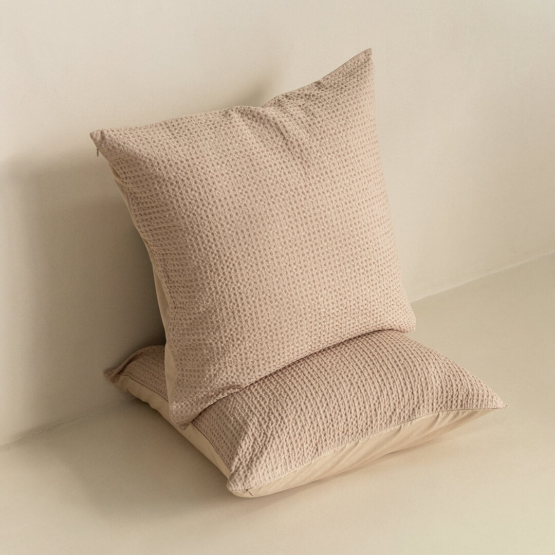 Two beige textured pillows on a light surface with a neutral background.