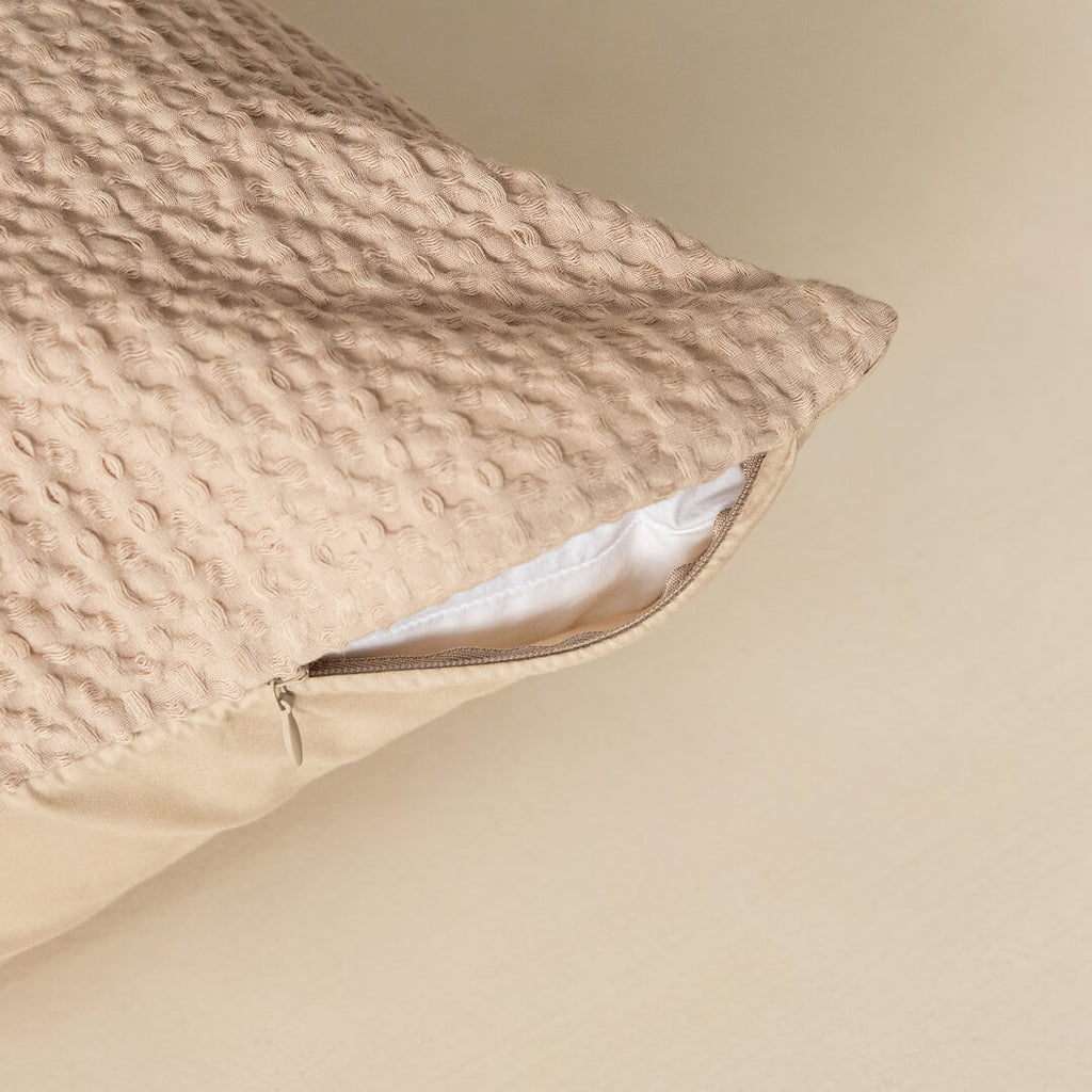 Textured beige pillow with a zipper on a beige background.