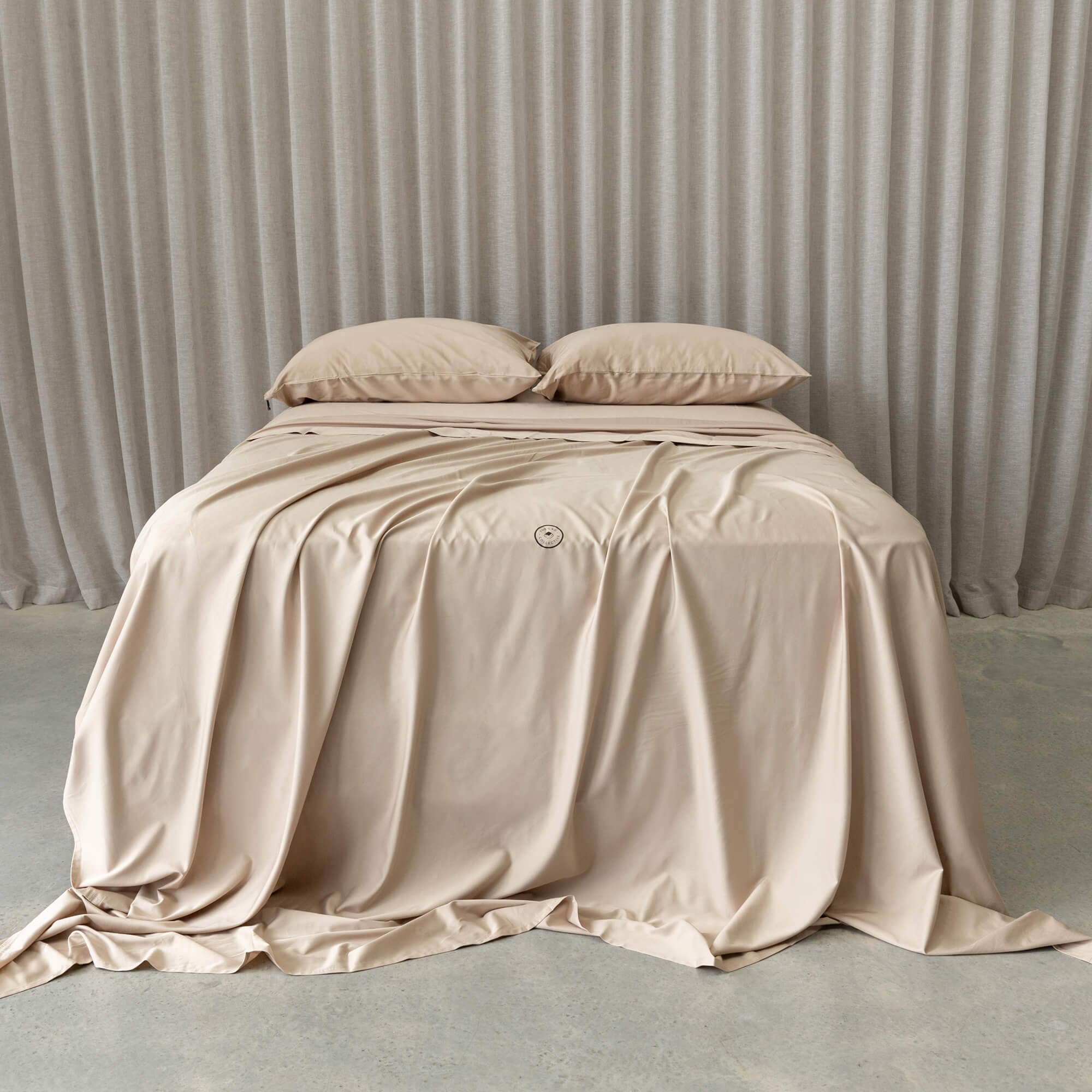 Beige bedding set shown on bed with a curtain in the background. 