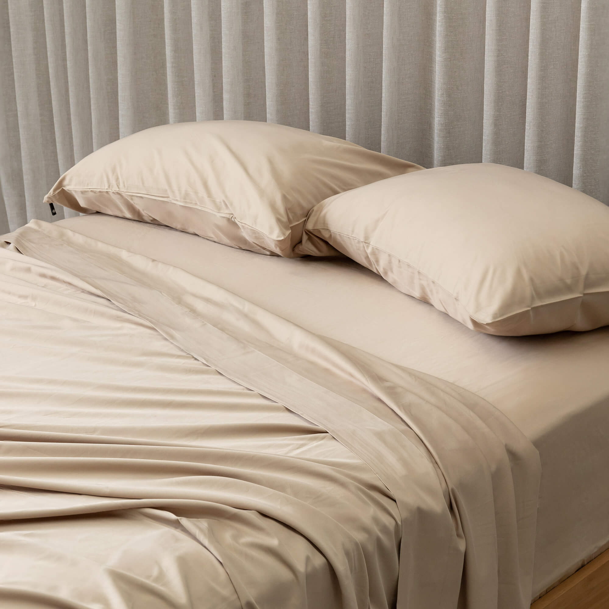 Beige bedding set shown on bed with a curtain in the background. 