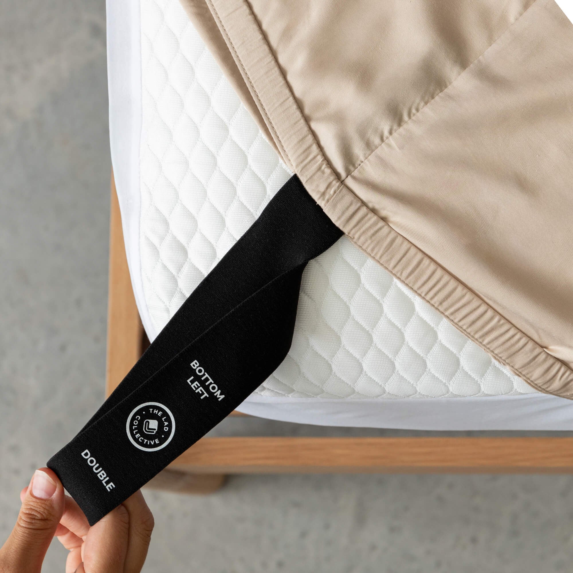 Labelled loop corner strap being pulled by a hand on fitted sheet that says 'Bottom Left', 'Double'.