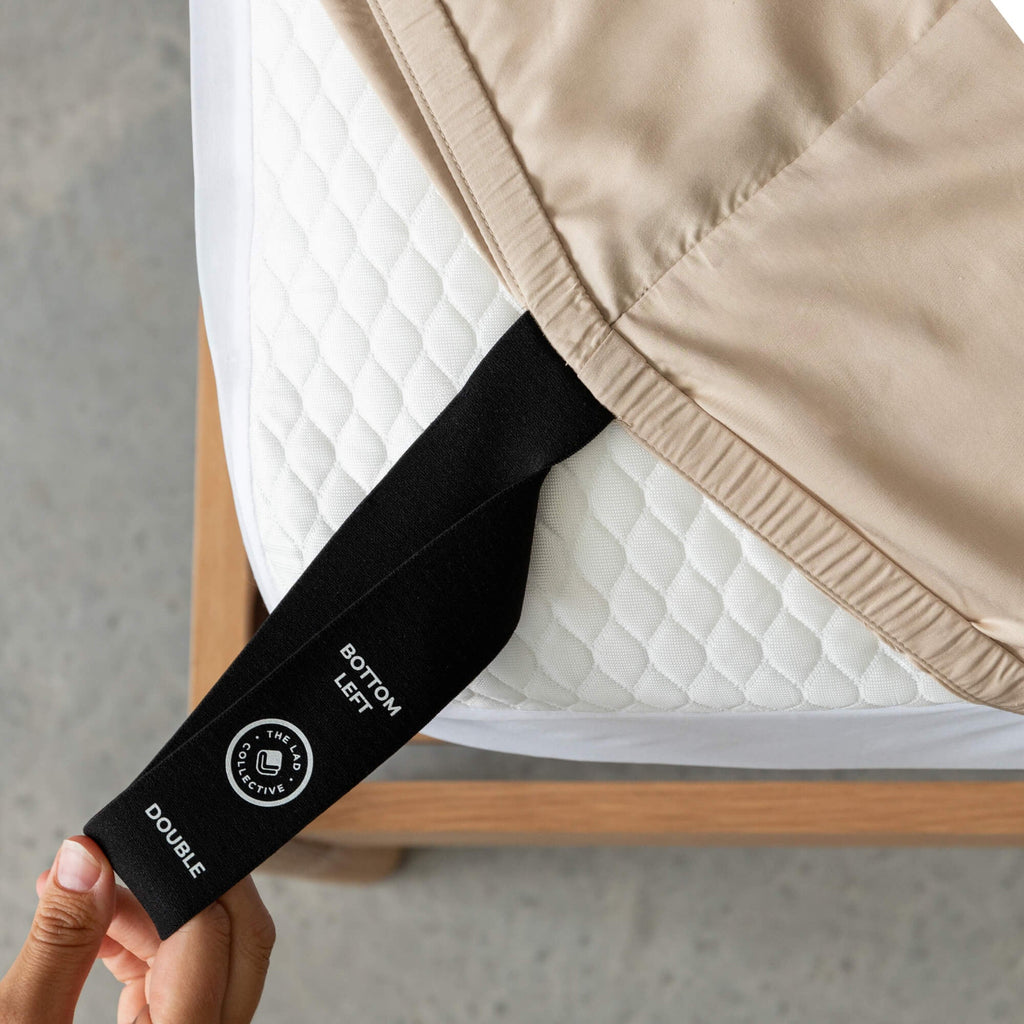 Labelled loop corner strap being pulled by a hand on fitted sheet that says 'Bottom Left', 'Double'.