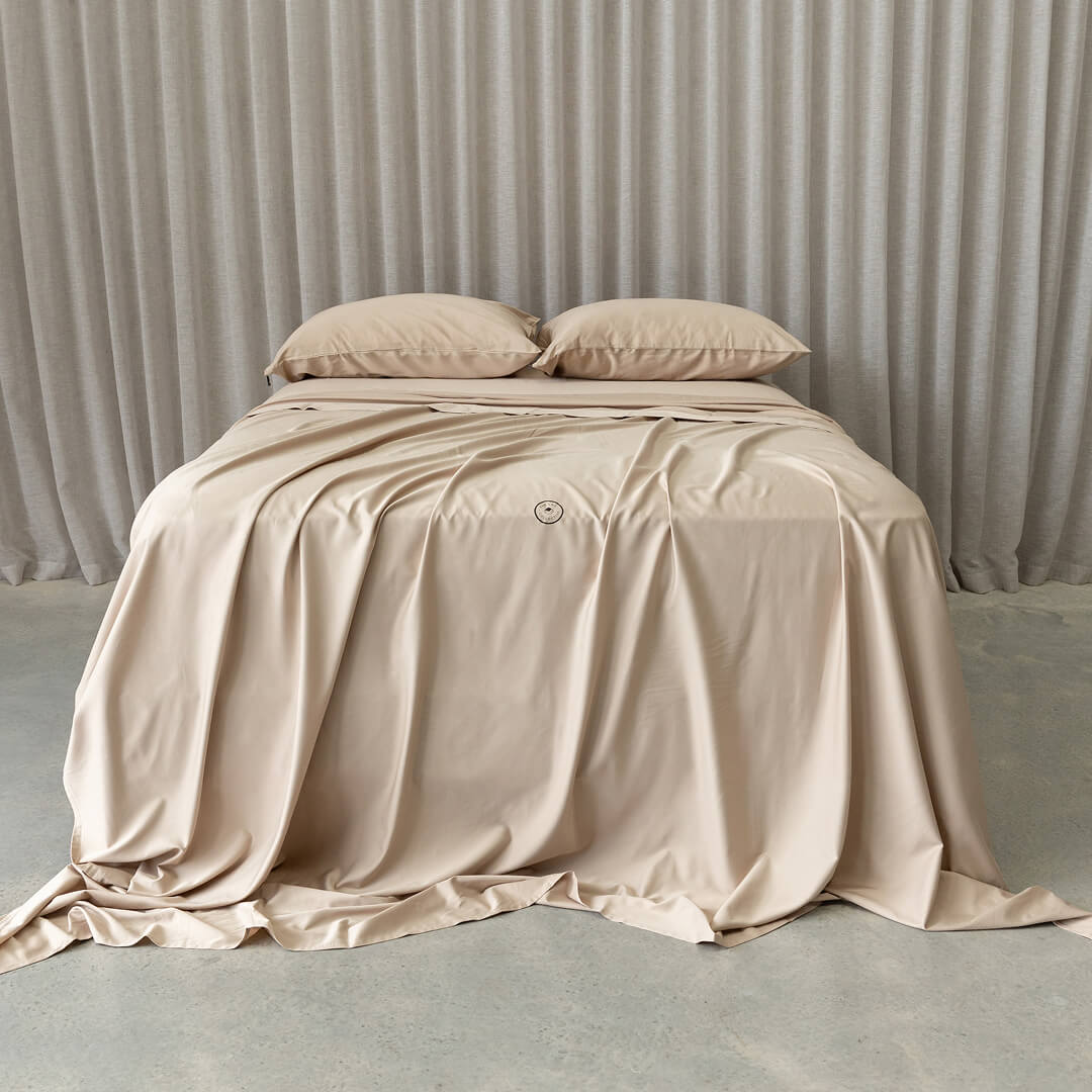 Beige bedspread with pillows on a bed against a neutral background.