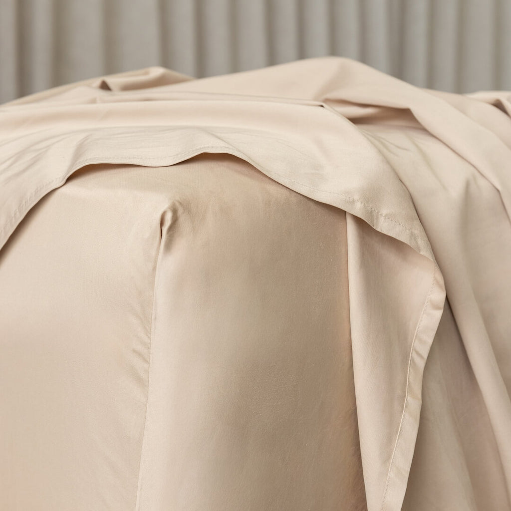 Beige bed sheets draped over a bed with a neutral background.