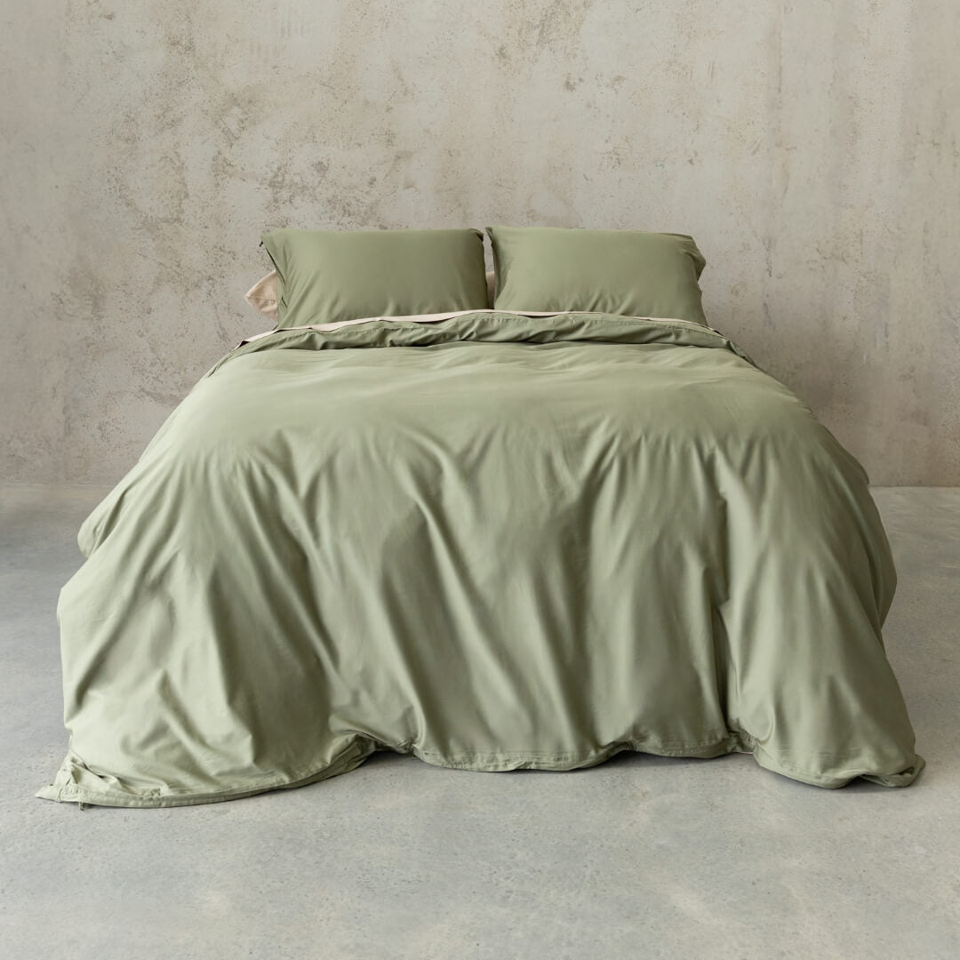 Sage green quilt cover set on a bed, against a neutral concrete look backdrop.