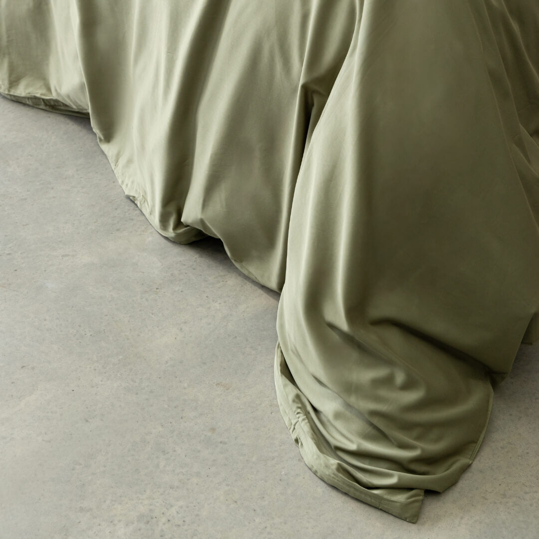 Sage green quilt cover magnetic close-up, draped over bed.