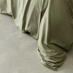 Sage green quilt cover magnetic close-up, draped over bed.