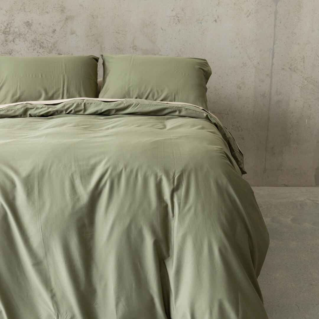 Sage green quilt cover set on a bed, against a neutral concrete look backdrop.